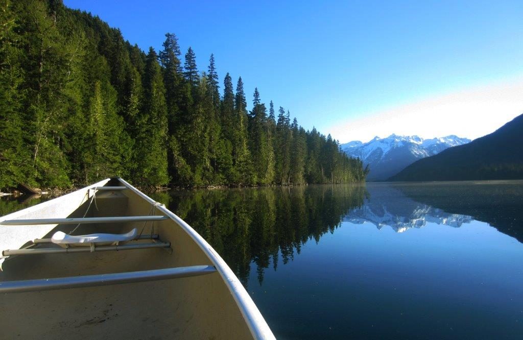 Canoe available for paddle sports rental floating on the glass-like surface of Birkenhead Lake, with rugged mountains in the background.
