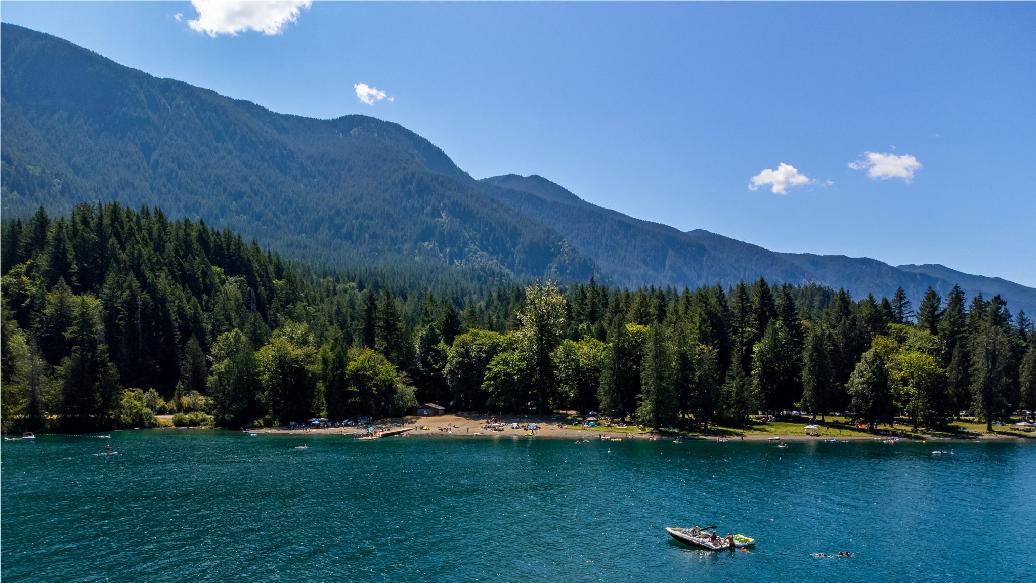 Sunny day at Cultus Lake with swimmers and boater enjoying the clear water near the beach.