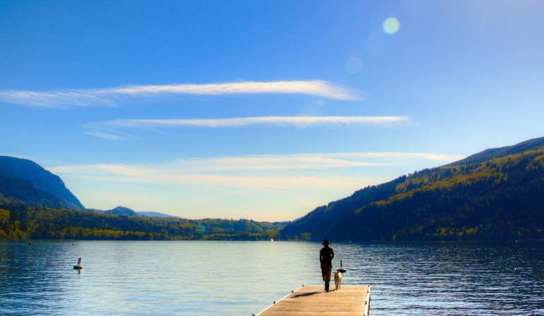 Image of person and dog walking along dock with a background of Cultus Lake and surrounding mountains.