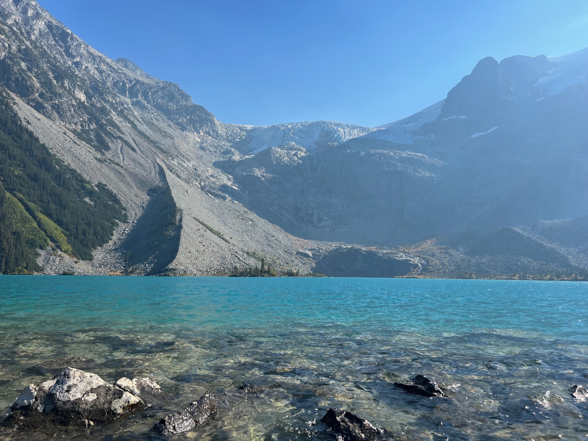 Panoramic view of the vibrant turquoise glacier-fed water at Joffre Lakes Provincial Park under a clear blue summer sky.