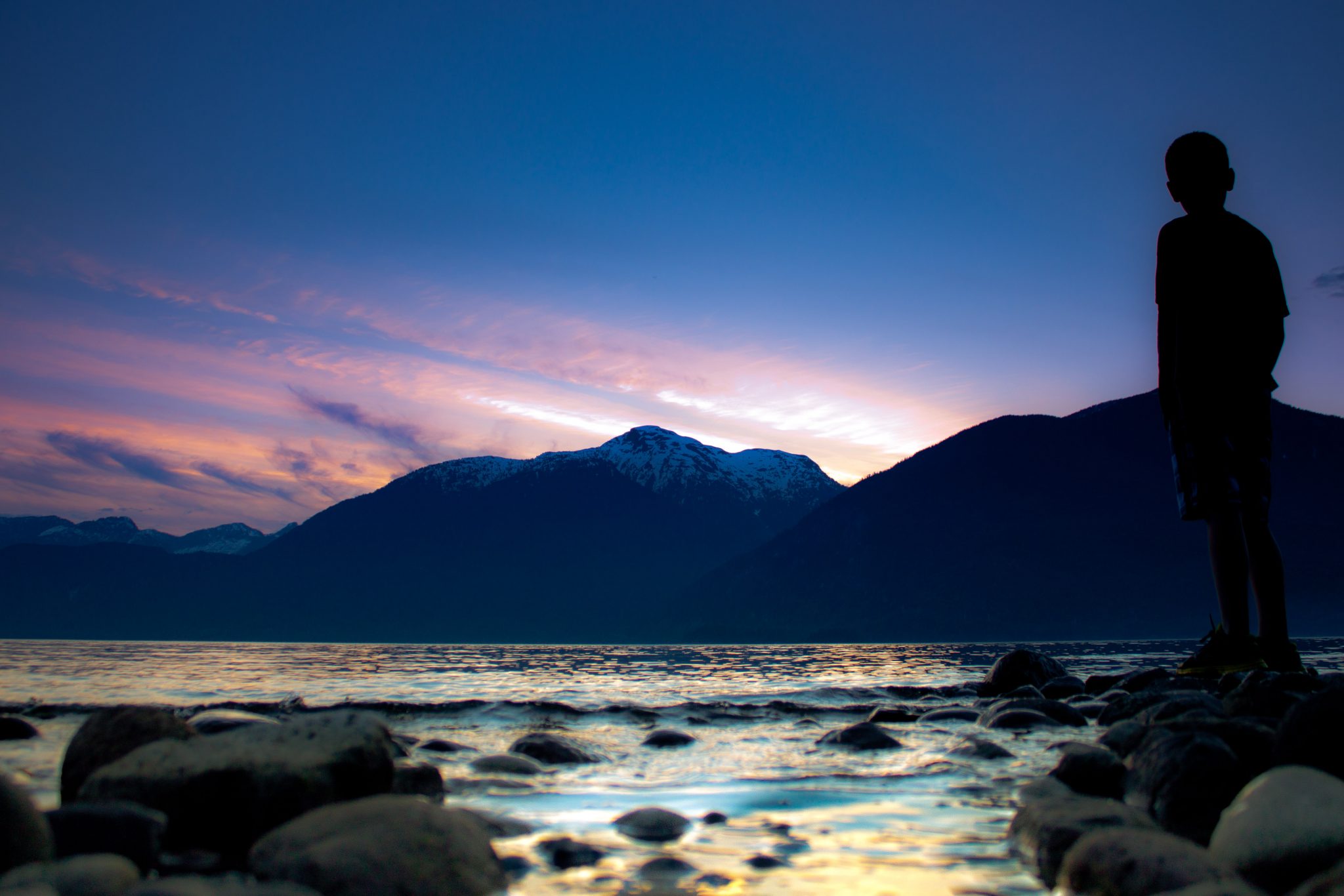 Person standing on the shoreline at Porteau Cove Provincial Park, silhouetted against the ocean during a colorful sunset