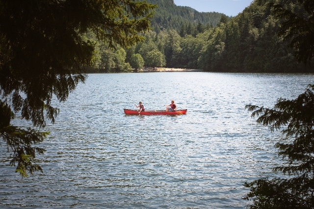 Two people enjoying a paddle sport rental while canoeing on the calm waters of Alice Lake, surrounded by dense evergreen trees.