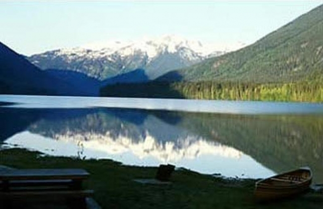 Mirror-like reflection of rugged, snow-capped mountains on the calm surface of Birkenhead Lake in Birkenhead Lake Provincial Park, BC.