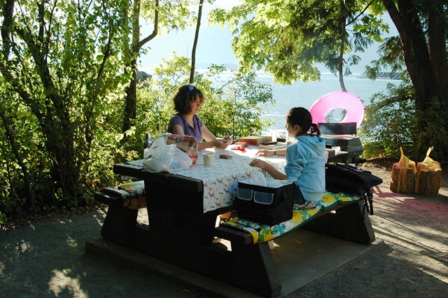 Family enjoying a picnic lunch at a designated campsite in Porteau Cove Provincial Park, surrounded by trees and coastal views.